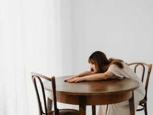 mujer-sentada-en-una-silla-de-madera-al-lado-de-una-mesa-pensativa