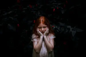 niña-pelirroja-con manos-en-el-rostro-y-fondo-oscuro